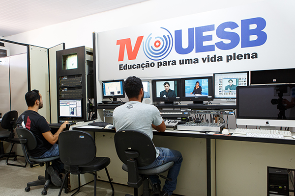 Técnicos de edição sentados em frente à ilha de edição, com muito computadores. 