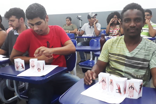 Sala de aula com cerca de dez estudantes, entre homens e mulheres, sentados em carteiras azuis durante o curso sobre a Escrita SEL.