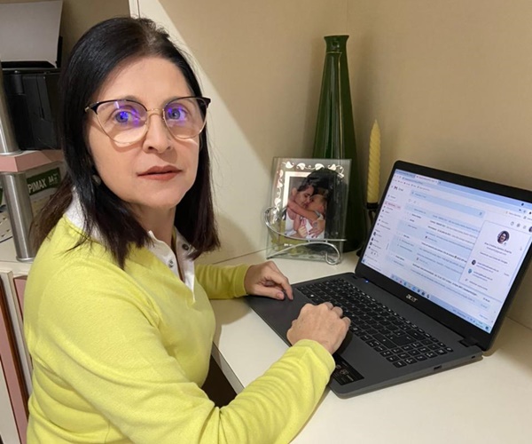 Professora Ana Cristina Duarte sentada à frente do computador realizando orientação da Escola de Pesquisadores.
