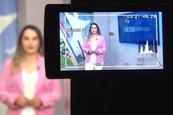 Imagem com a apresentadora do Uesb Notícias 2ª edição, Aline Ferraz. Ela está no estúdio da TV em apresentação do telejornal.