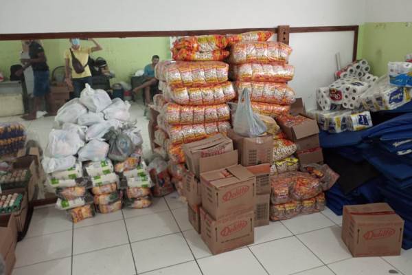 Fardos de alimentos, caixas com mantimentos, embalagens de papel higiênico e sacolas numa sala de aula da Uesb.