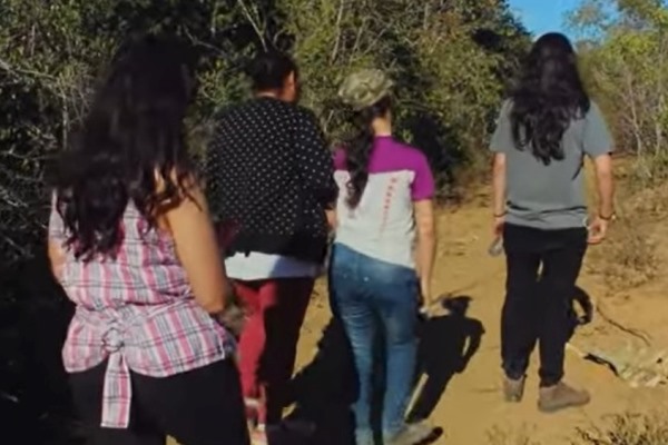 Quatro pessoas caminham pela estrada de chão, eles estão de costas para a imagem.